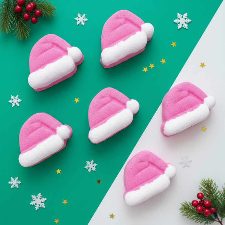 Red Santa hat bath bombs with white trim on a green and white background with Christmas decorations.