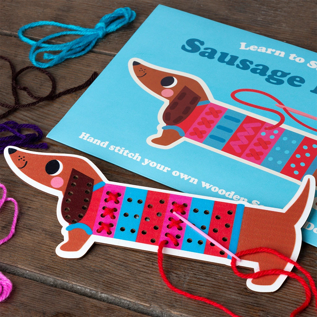 Wooden Sausage Dog Learn to Sew Kit contents laid out on a table - includes stitch board, needle, and colourful yarn