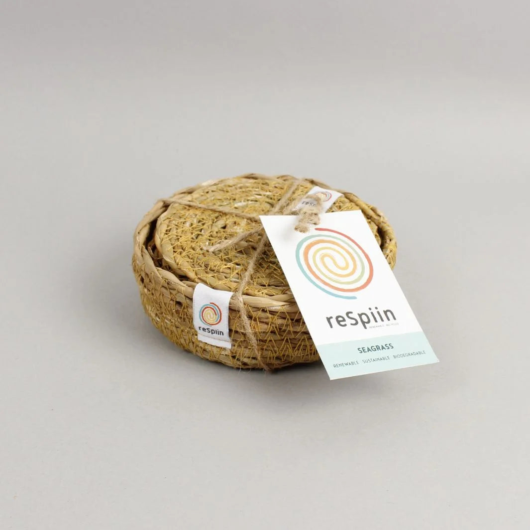 set if round seagrass coasters in a matching woven holder. Placed on a grey background