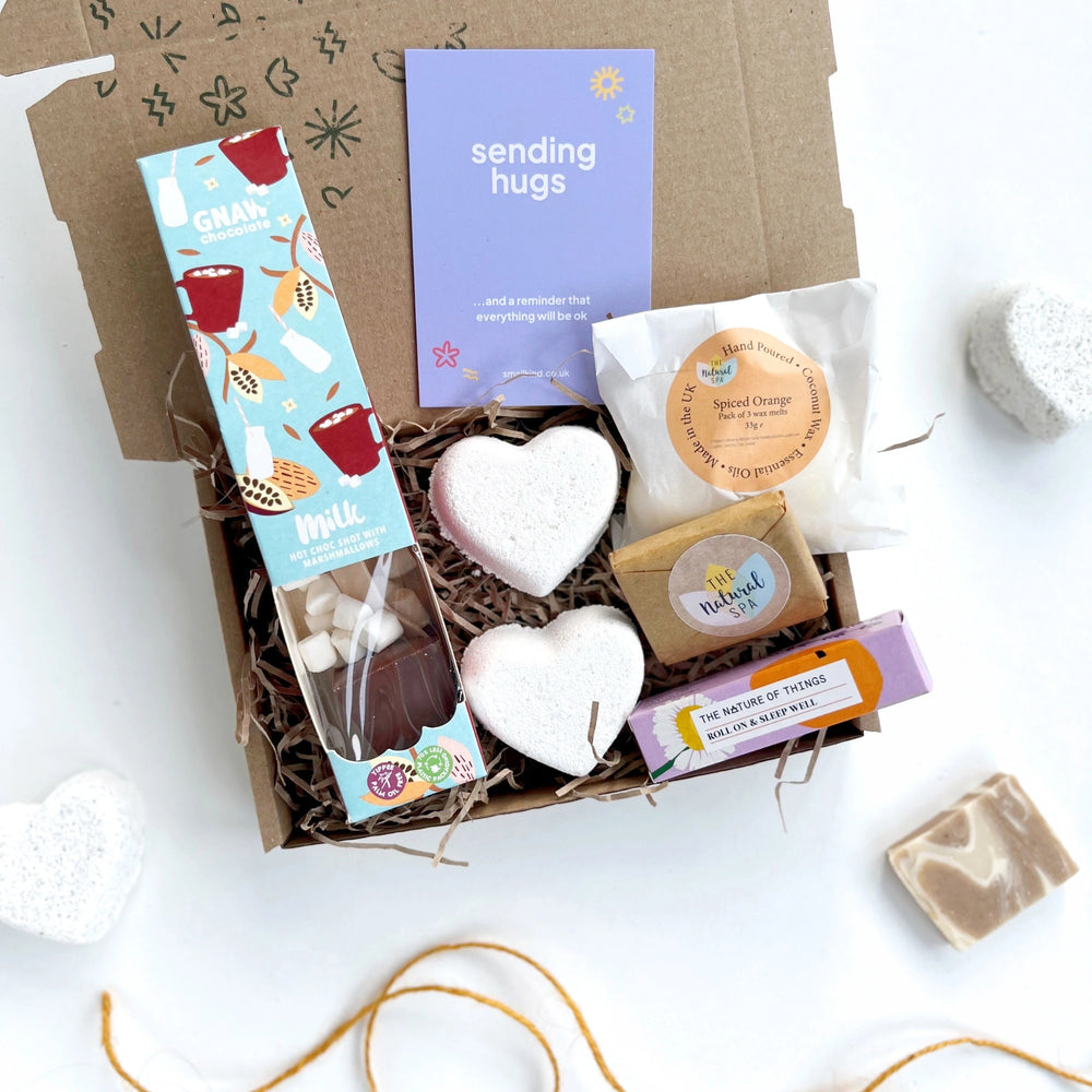 sending hugs gift box with a hot chocolate stirrer, two natural bath bomb hearts, spiced orange wax melts, natural face wash bar and an aromatherapy pulse point roller. The products are inside a hand stamped kraft gift box with a card that reads 'sending hugs' 