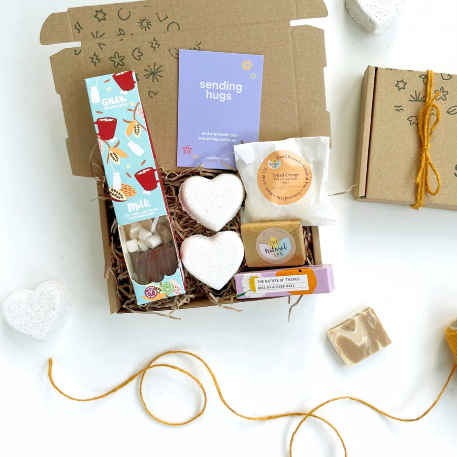 sending hugs gift box with a hot chocolate stirrer, two natural bath bomb hearts, spiced orange wax melts, natural face wash bar and an aromatherapy pulse point roller. The products are inside a hand stamped kraft gift box with a card that reads 'sending hugs' 