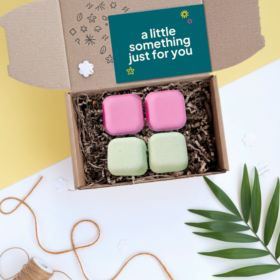 Box of colourful shower steamers with a card reading 'a little something just for you' on a decorative background.