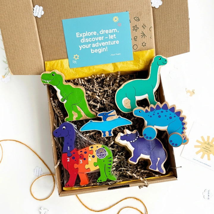 Box of colourful wooden dinosaur toys with a card on top which says 'explore, dream discover - let your adventure begin.