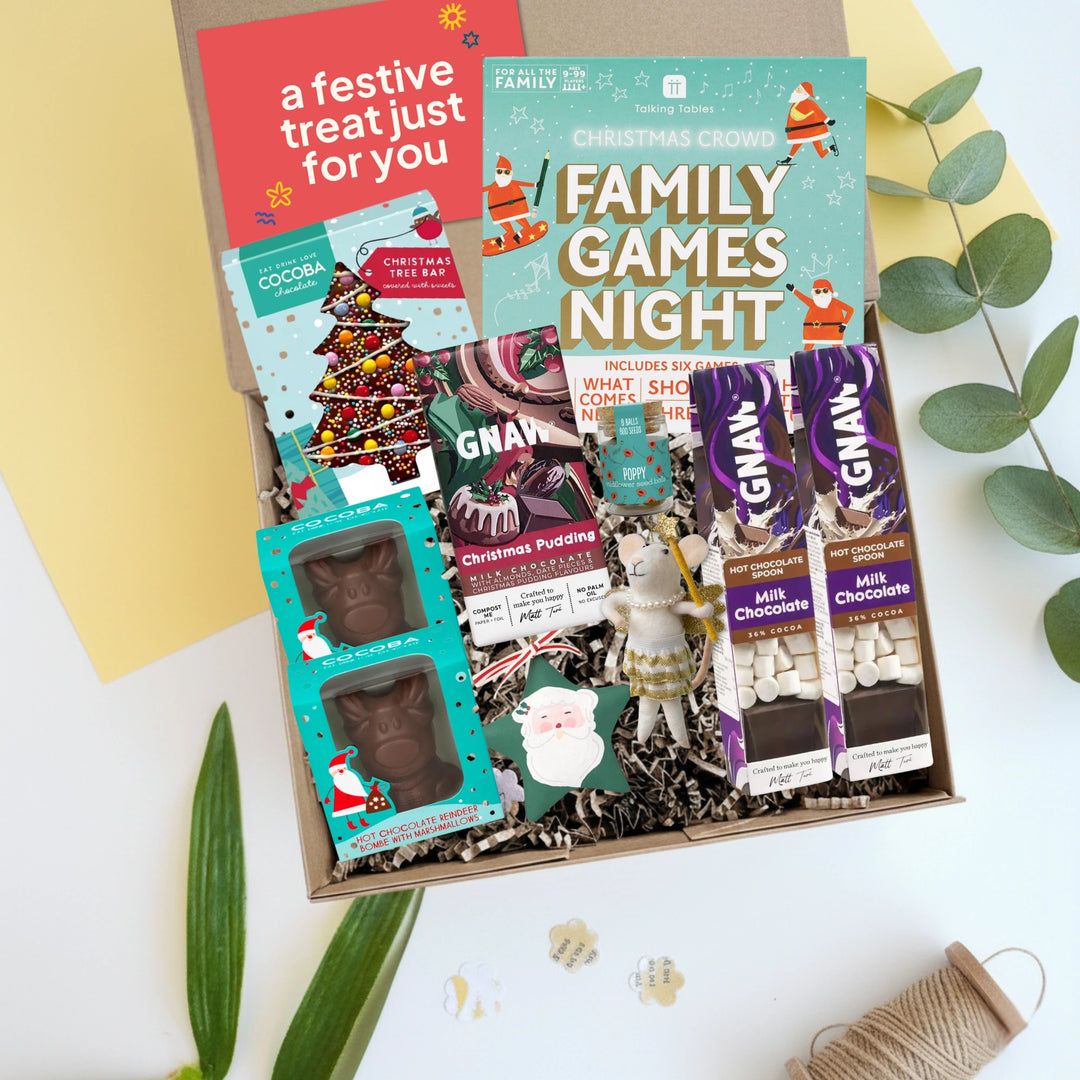 smallkind family Christmas Hamper gift set with chocolate bars and games on a white surface with green leaves.