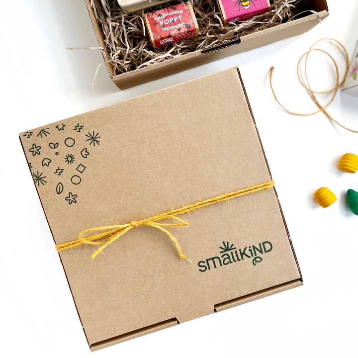 smallkind square kraft gift box hand stamped with the smallkind logo and pattern in green. The box is tied with mustard yellow twine. 