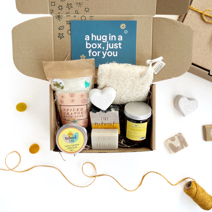 smallkind spa day pamper box including spiced orange bath soak, a natural bath bomb heart, spiced orange soap bar, face wash bar, lemon sorbet candle in a glass jar. The products are inside a hand stamped gift box with a card which reads 'a hug in a box, just for you'