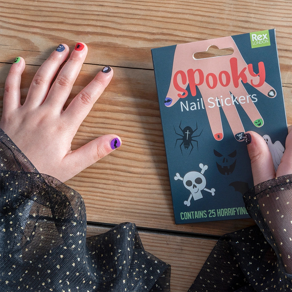 Girls hands with Halloween-themed nail stickers on a wooden surface next to a package of 'Spooky' nail stickers.