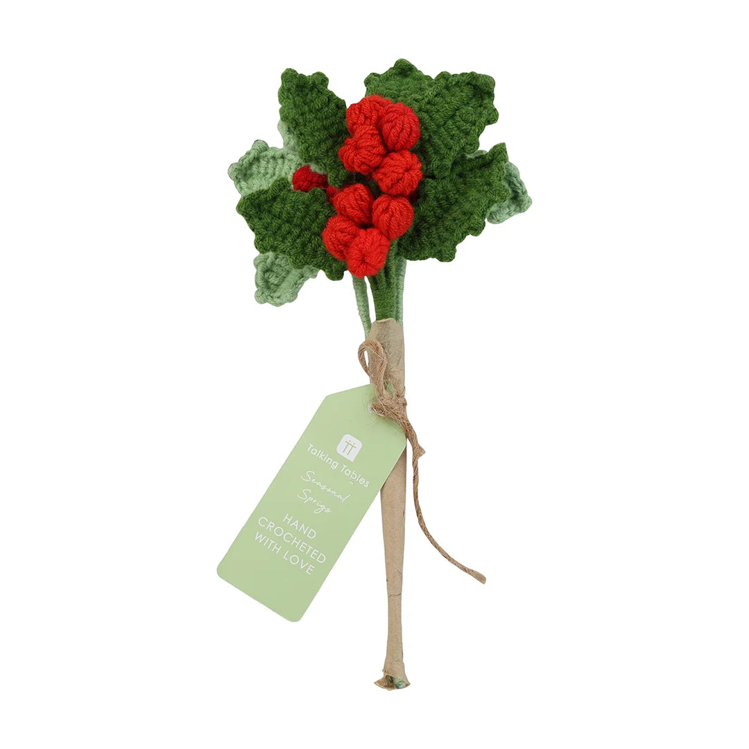 Handmade crocheted holly branch with red berries and green leaves on a white background.