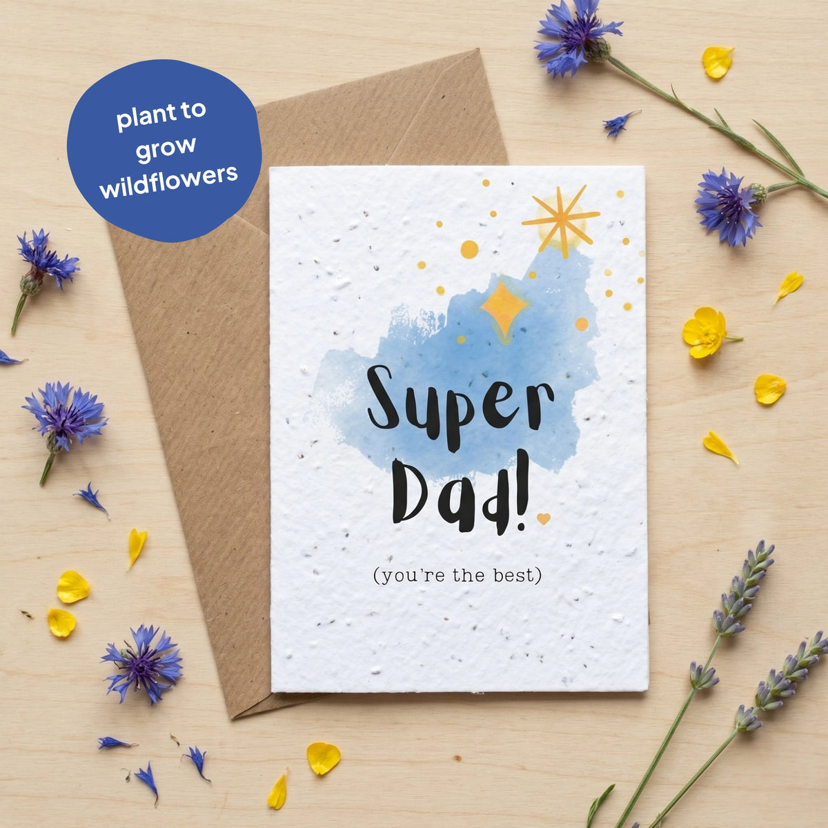 Greeting card with 'Super Dad!' text and plantable seeds, surrounded by flowers on a wooden surface.