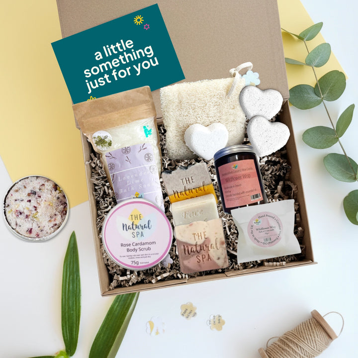 Luxury Pamper Hamper Gift box with natural spa pampering products including soap bars, candle, wax melts, loofah and body scrub on a white background with decorative leaves 