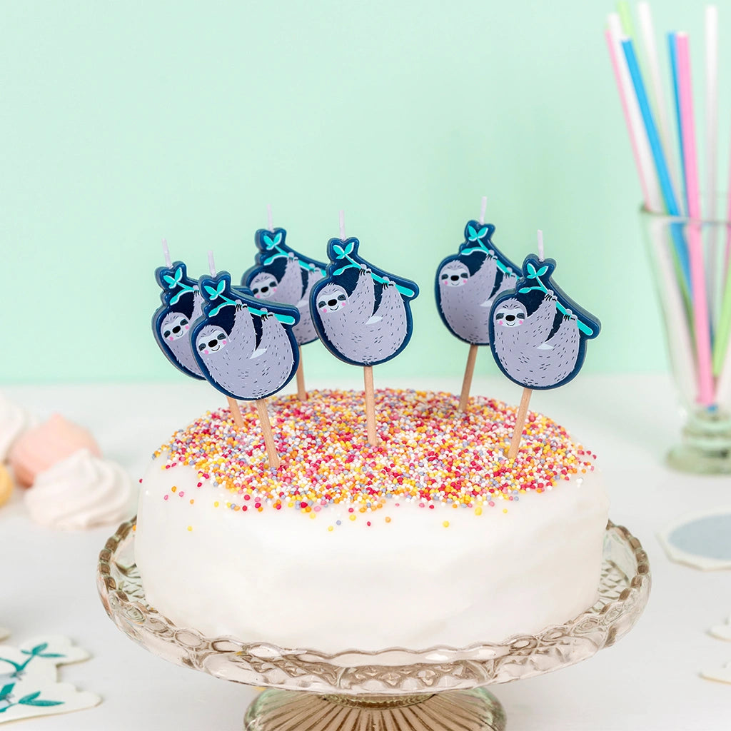 Cake with sloth-themed candles on a white cake with rainbow sprinkles against a light green background