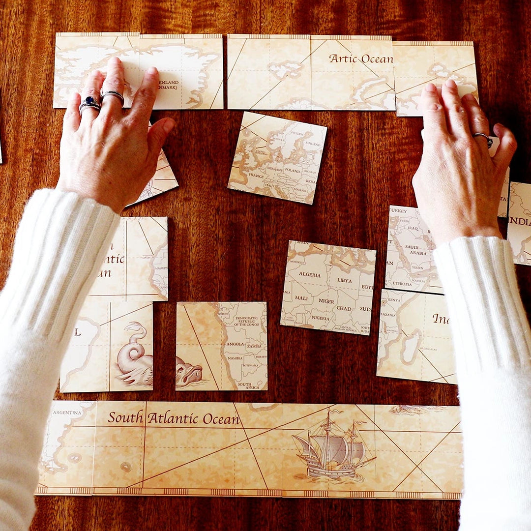 Hands arranging vintage-style world map cards on a wooden surface