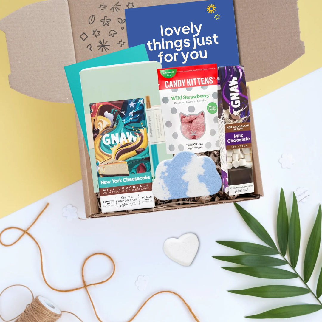 An open gift box arranged in a flat lay with a blue card reading &