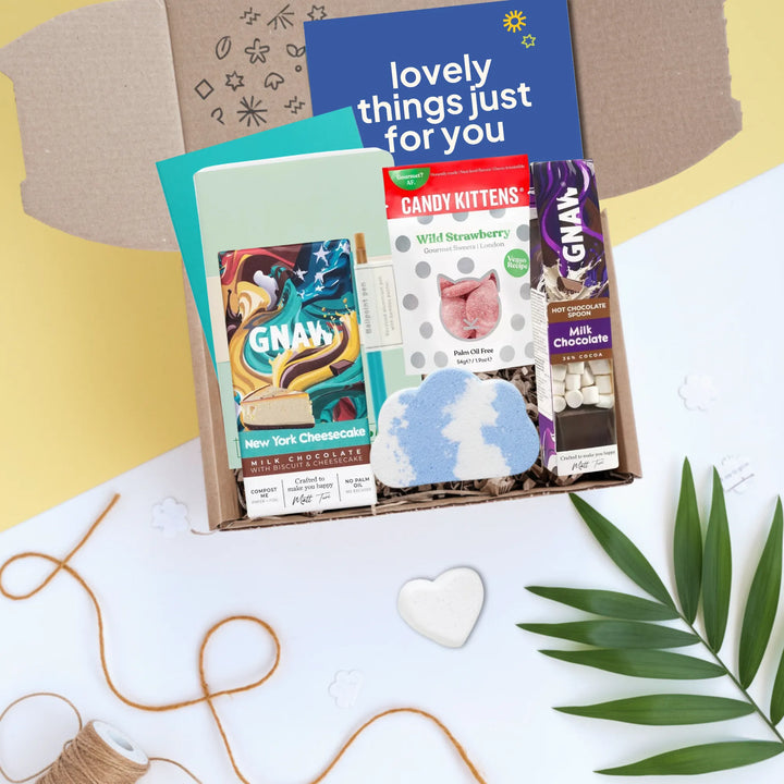 An open gift box arranged in a flat lay with a blue card reading &