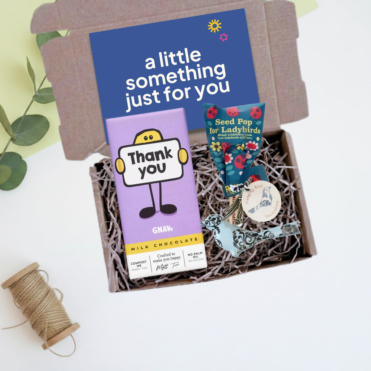 Gift box with chocolate bar, seed pop,  metal bird decoration and a gift card on a light background 