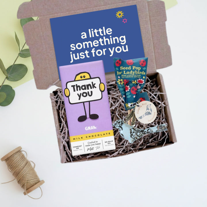Gift box with chocolate bar, seed pop,  metal bird decoration and a gift card on a light background 
