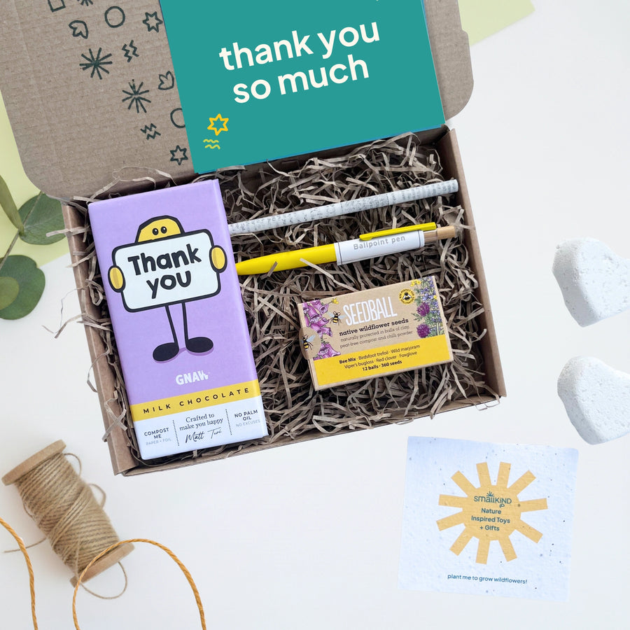Gift box with chocolate, pen, pencil and seed box labeled 'thank you so much' on a light background.