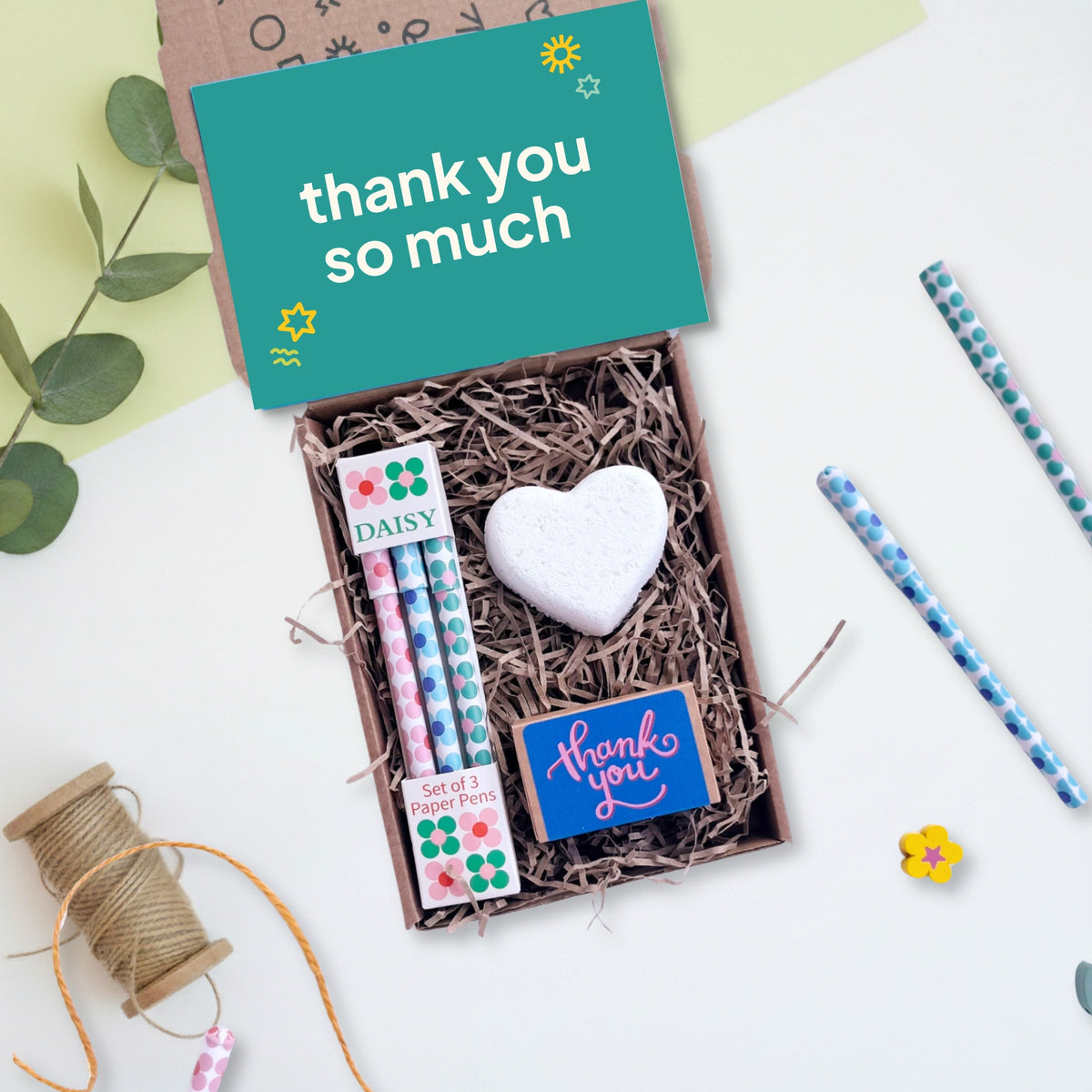 Gift set with pens, heart-shaped bath bomb, and 'thank you so much' card on a light background
