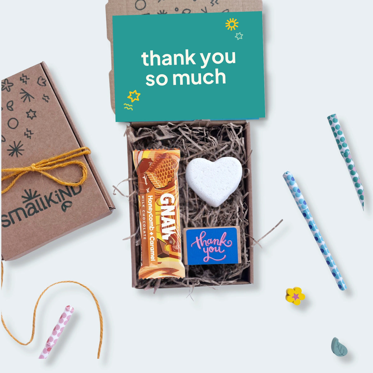Gift box with heart-shaped bath bomb, chocolate bar and a box of wildflower seedballs with 'thank you so much' card on a white background