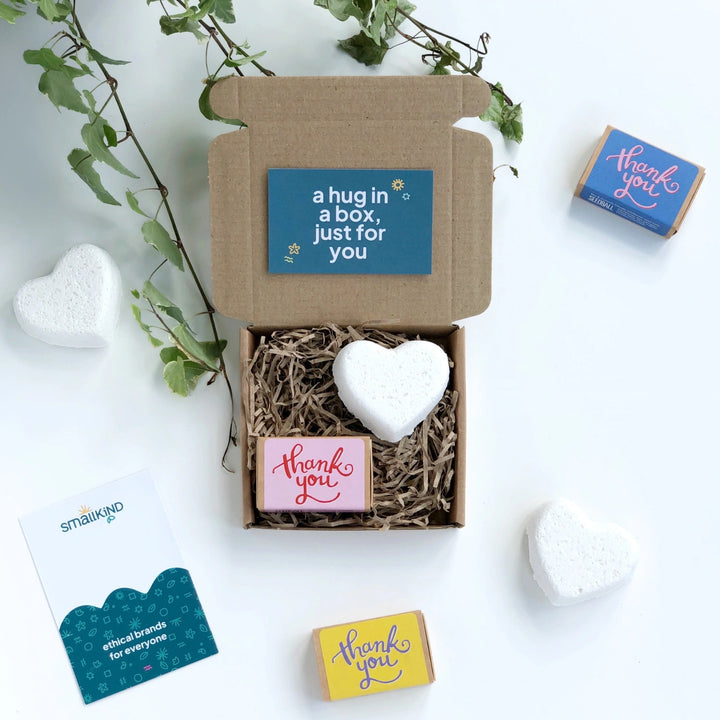 smallkind mini thank you box with a heart shaped bath bomb and a pink matchbox of seedballs printed with 'thank you' in red handwriting style text. The gift box has a dark green card resting on it which reads 'a hug in a box, just for you. 