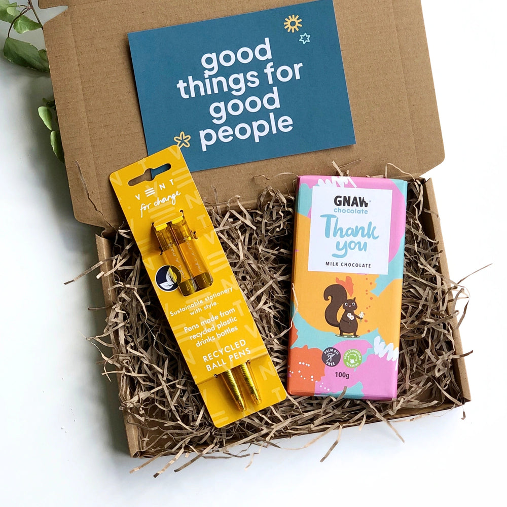 a bar of milk chocolate with colourful 'thank you' wrapping and a set of two yellow recycled pens. The products are inside a kraft gift box filled with shredded paper and a card which reads 'good things for good people'. This stationery gift box is perfect for colleagues, staff and teacher gifts.