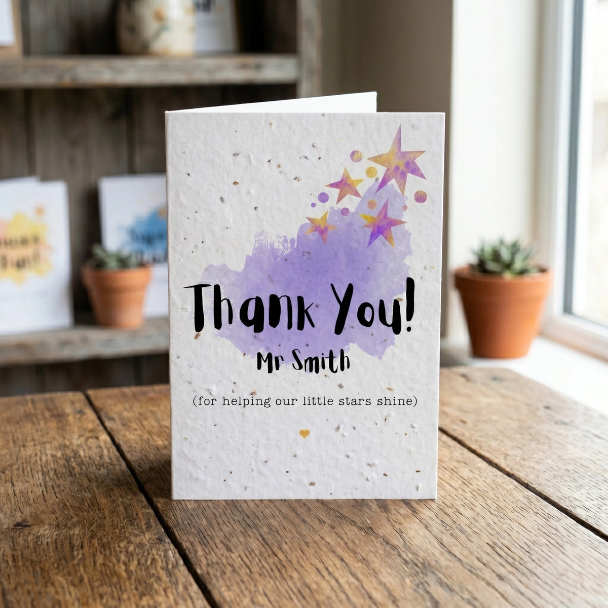 Greeting card with 'Thank You! Mr Smith' text on a wooden surface with plants in the background