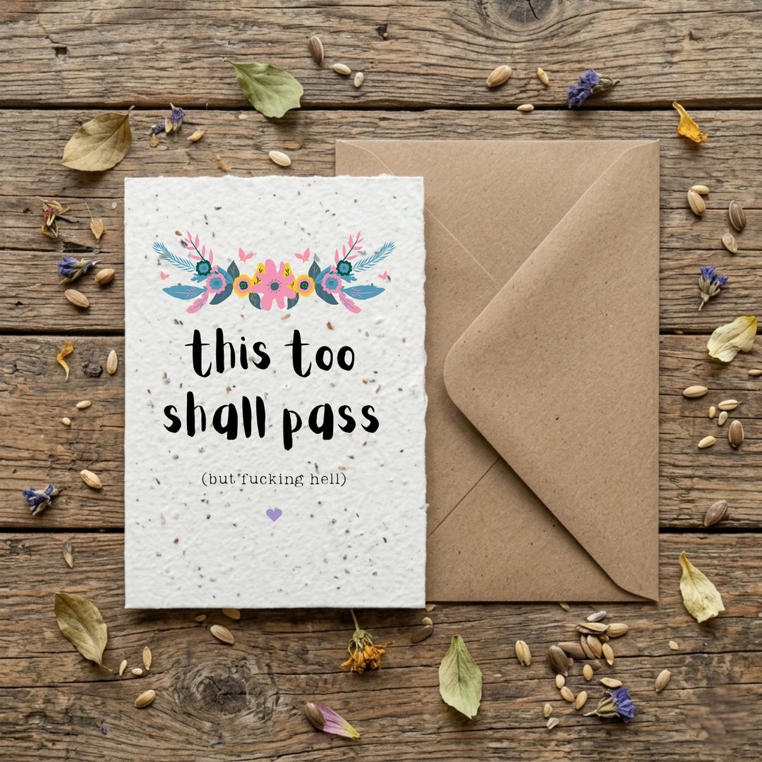 Greeting card with floral design and text on a wooden surface with an envelope and dried leaves.