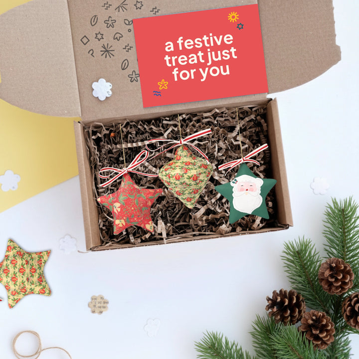 Box of upcycled decorative Christmas ornaments with a festive card on a white background