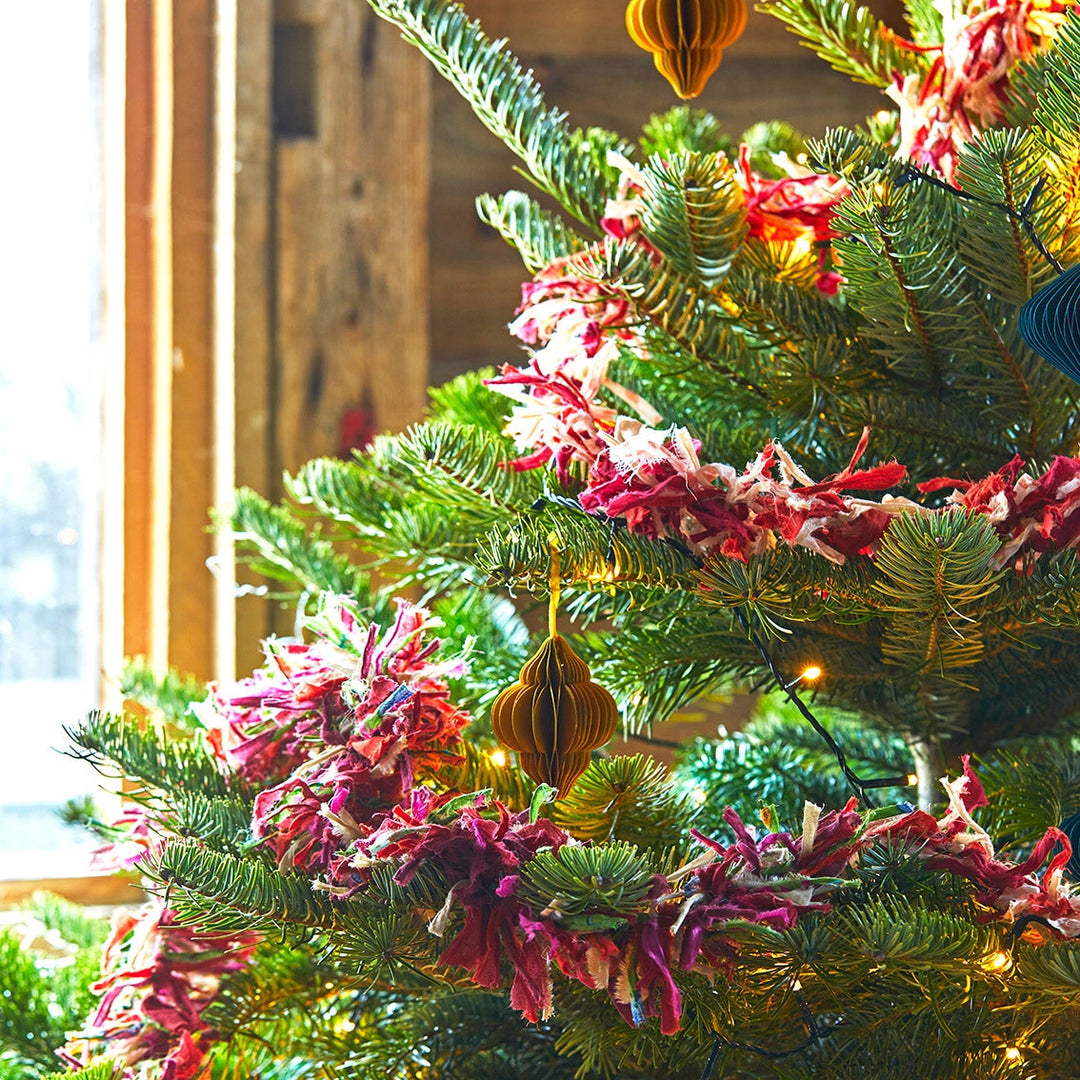 Decorated Christmas tree with colourful fabric tinsel and ornaments in a warm indoor setting.