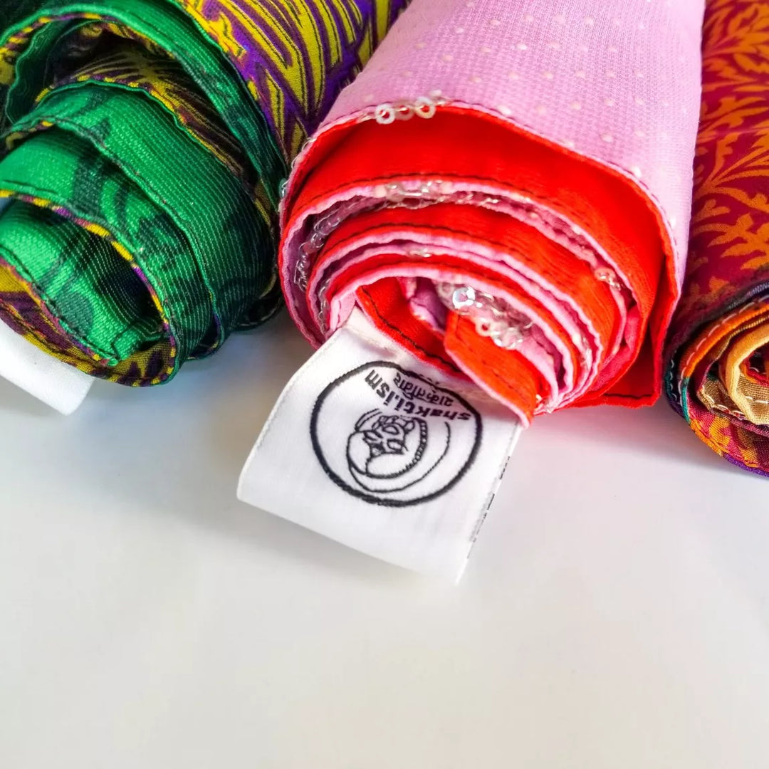 Rolls of colourful fabric gift wrap with a shakt.ism  brand label on a white background