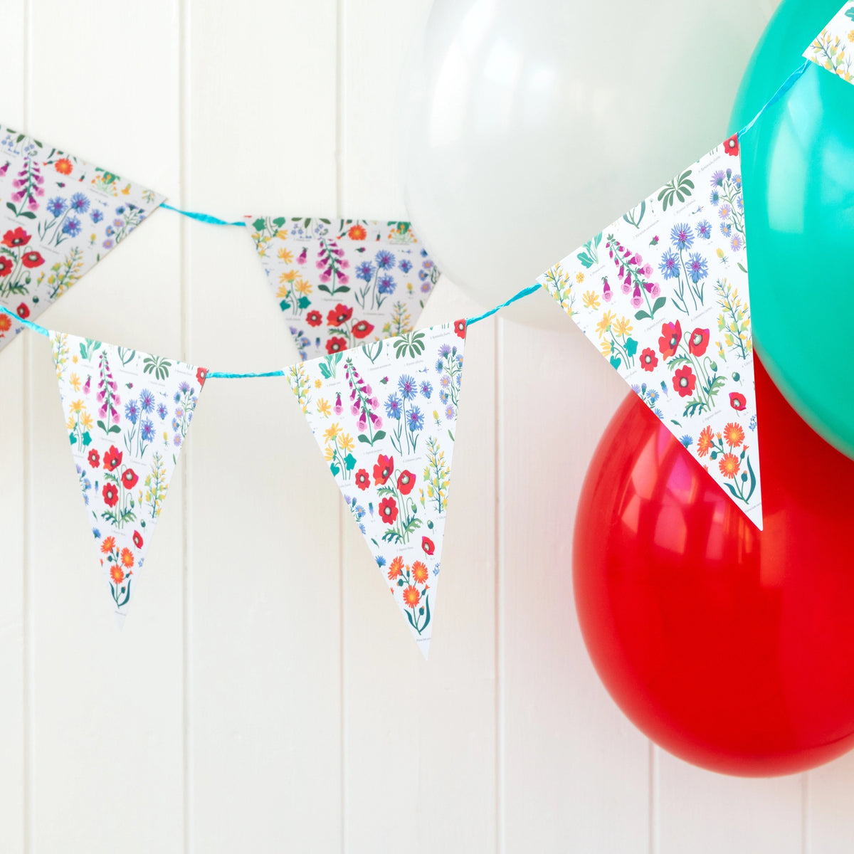  Wildflowers Party Bunting with colourful wild flowers print on a white background. Hung up with colourful balloons. 