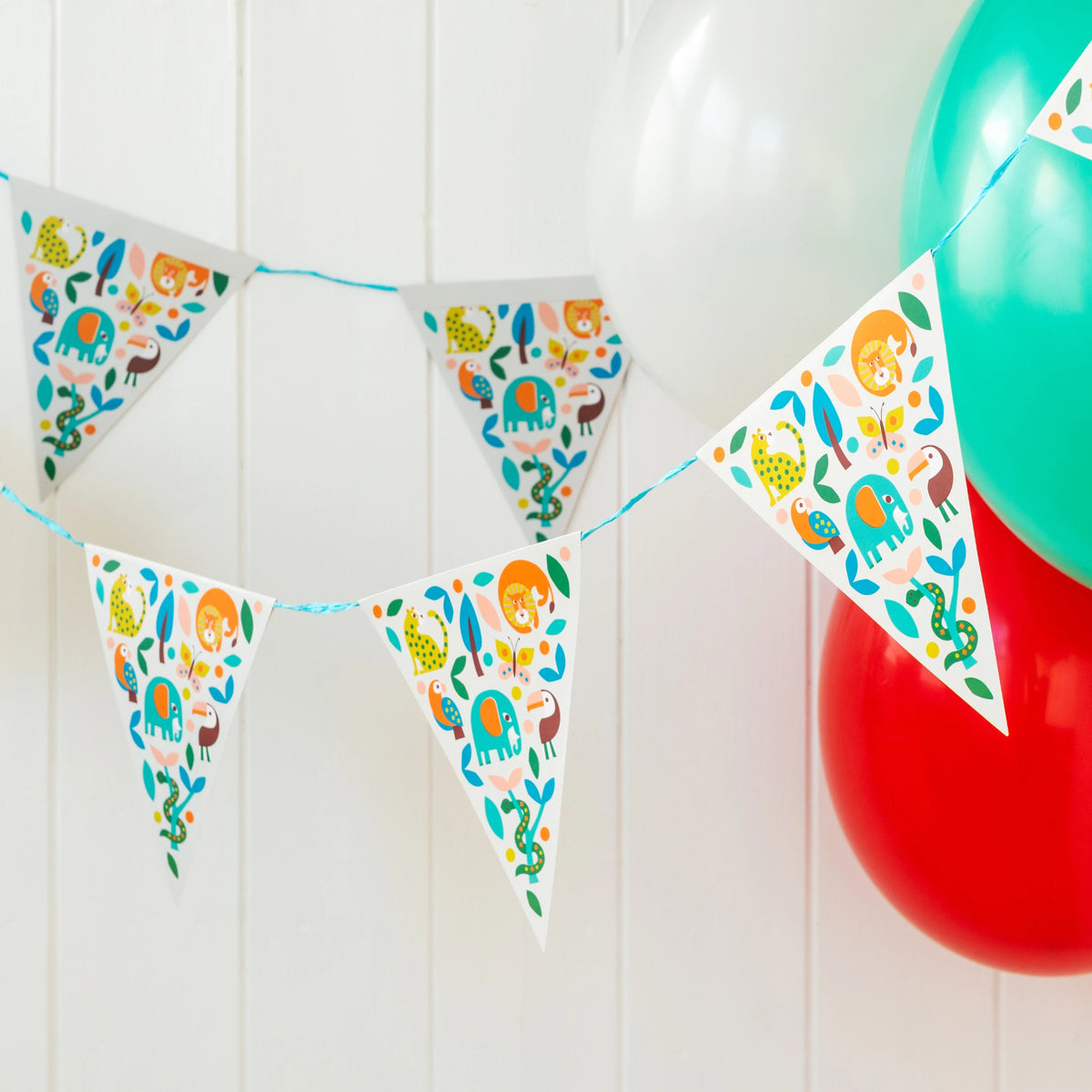 wild wonders party bunting with a colourful scandi style animal print on a white background. The bunting is hanging with colourful balloons styled for a party.