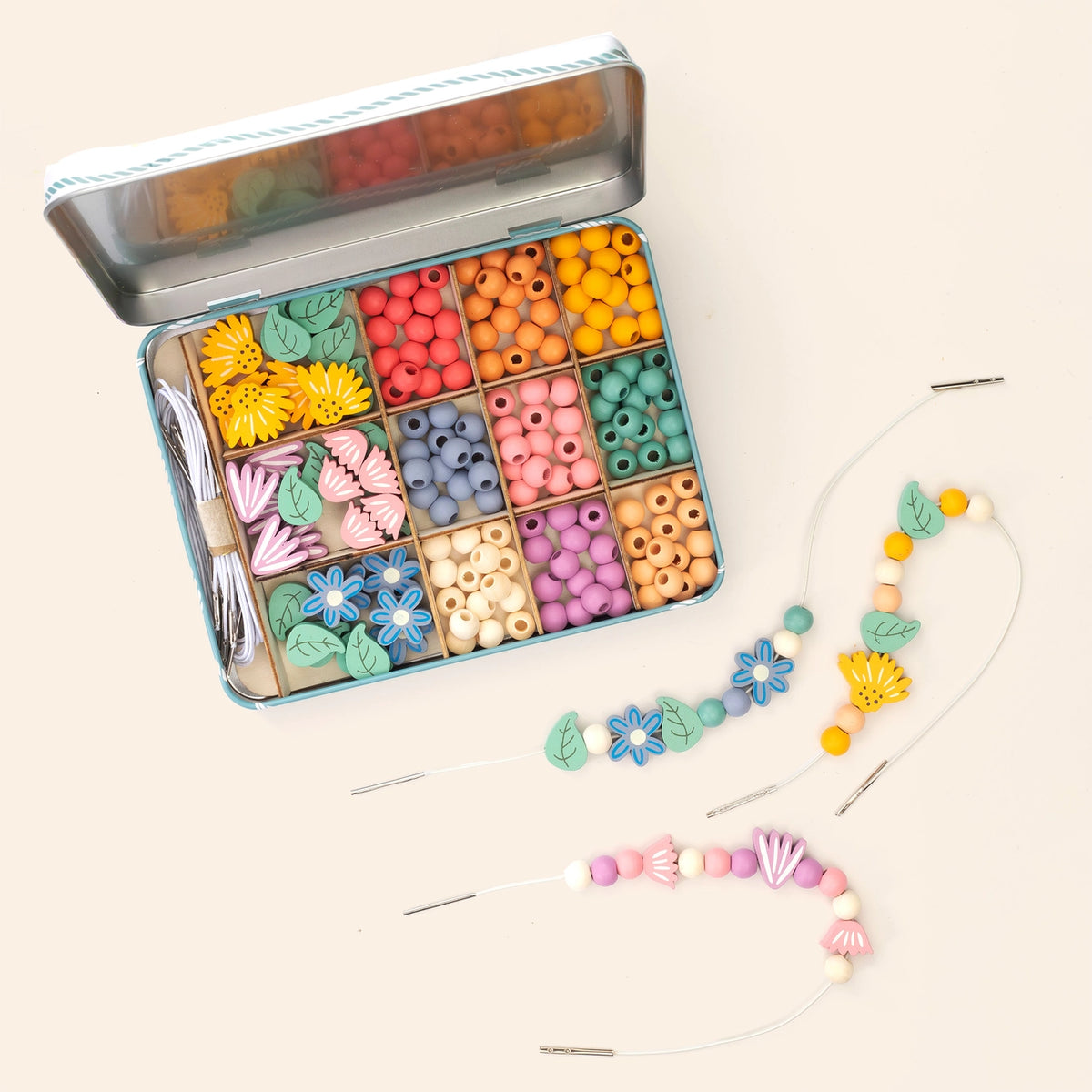 An open metal bead organizer box filled with colorful wooden beads, shown with two finished beaded bracelets on a light cream background.