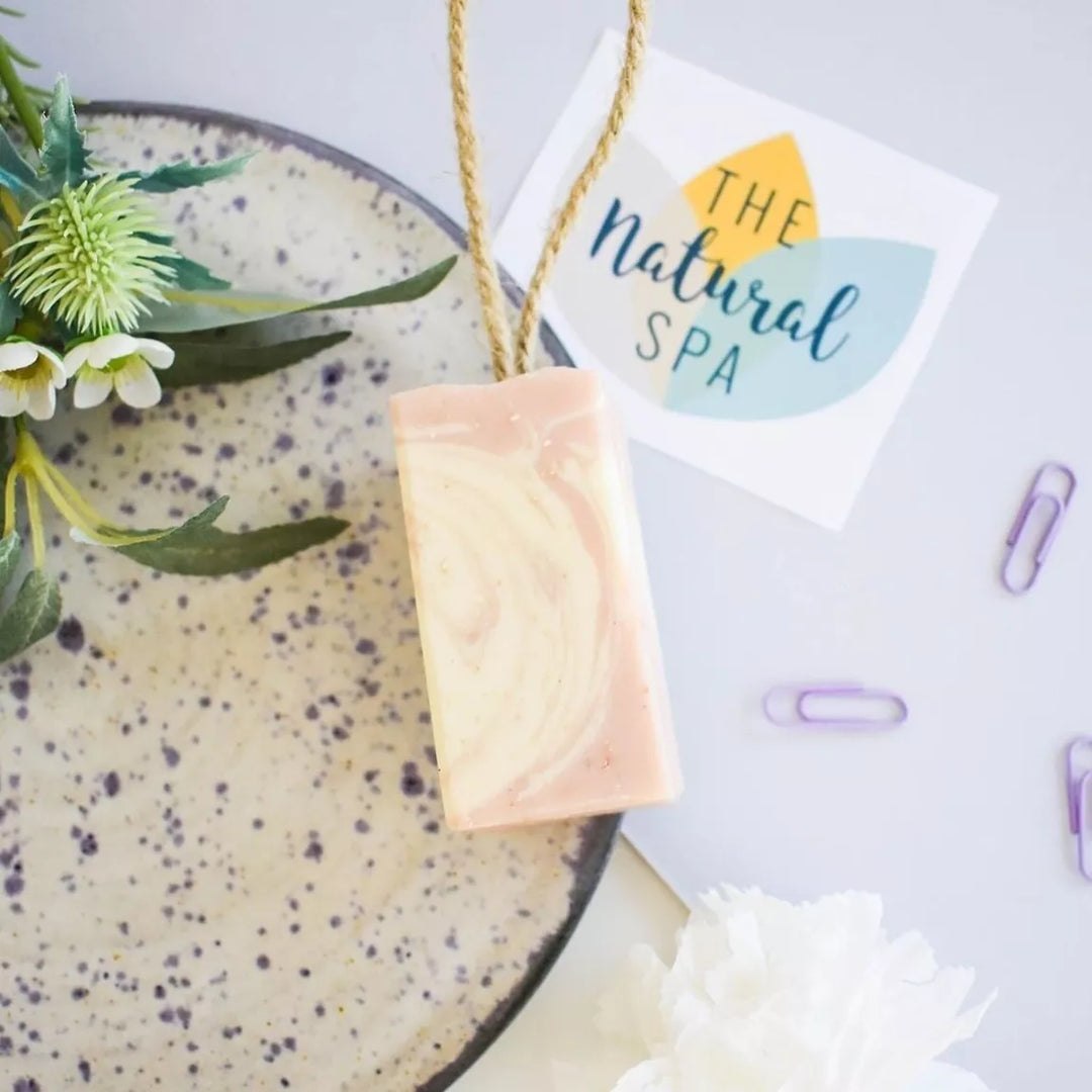 Bar of soap on a speckled plate with flowers and 'The Natural Spa' sign in the background