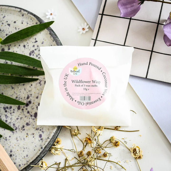 Pack of wildflower wisp wax melts with a pink label on a surface with flowers and leaves