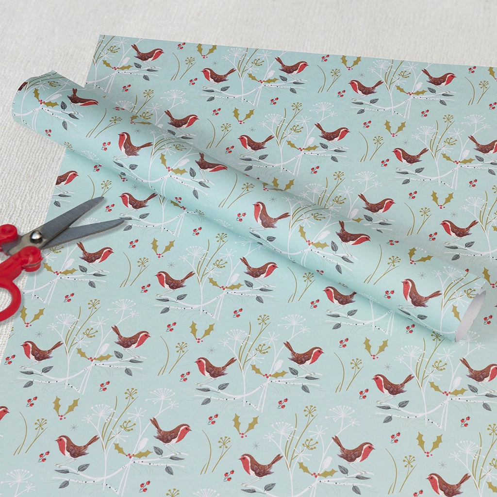 Roll of wrapping paper with bird and floral pattern on a light blue background, with scissors on top.