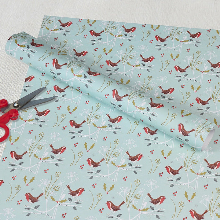 Roll of wrapping paper with bird and floral pattern on a light blue background, with scissors on top.