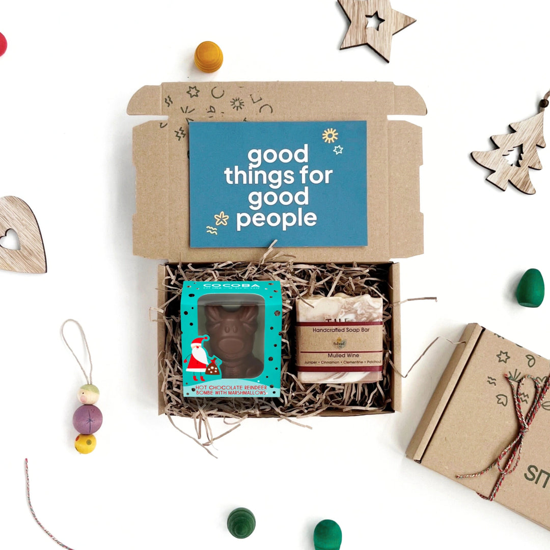 Gift box with 'good things for good people' card, reindeer hot chocolate bombe, and mulled wine soap on a white background