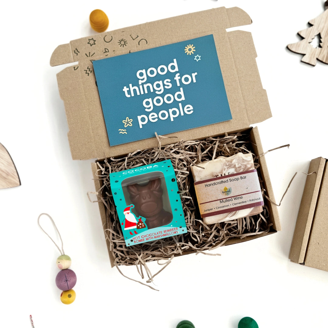 Gift box with 'good things for good people' card, reindeer hot chocolate bombe, and mulled wine soap on a white background