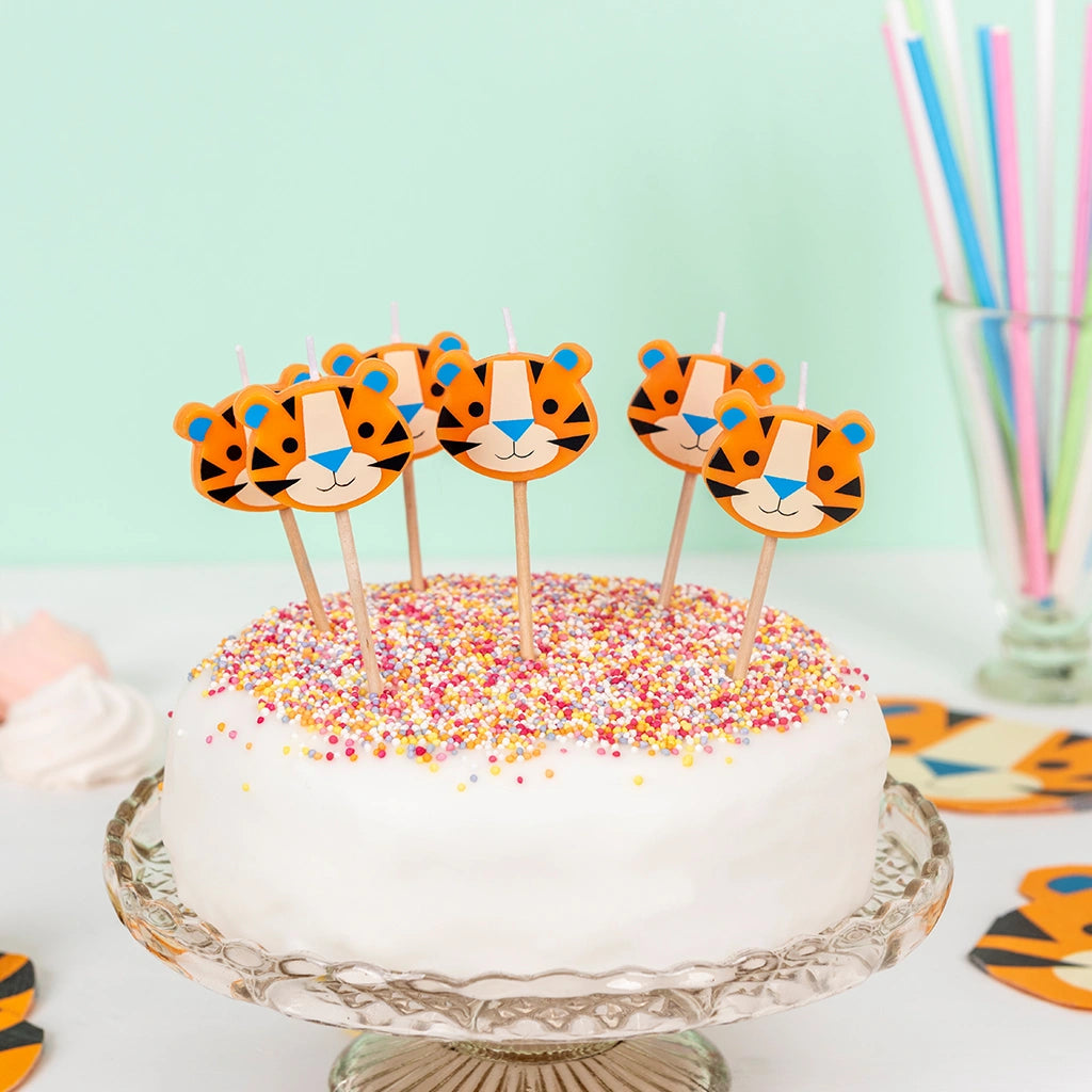 six Ziggy the Tiger, tiger shaped party candles on a white celebration cake with sprinkles