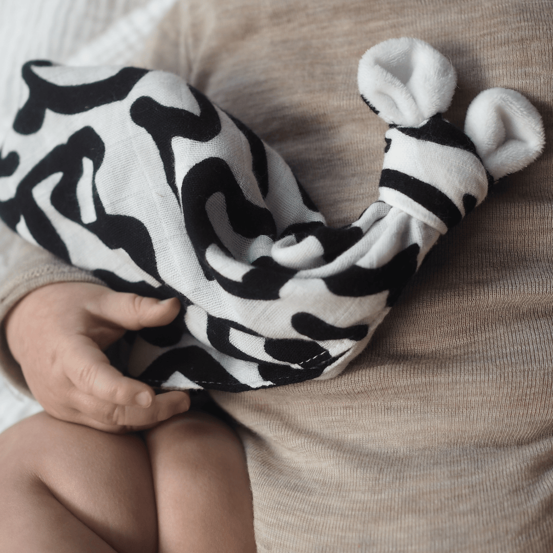 baby clutching an Etta Loves Bamboo Muslin Comforter in Keith Haring 'Baby' print