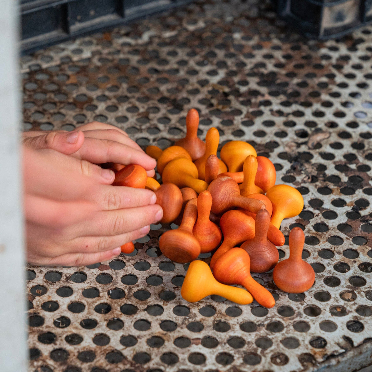 childs hands playing with a collection of small, wooden Grapat Mandala Pumpkins in various shades of orange and brown