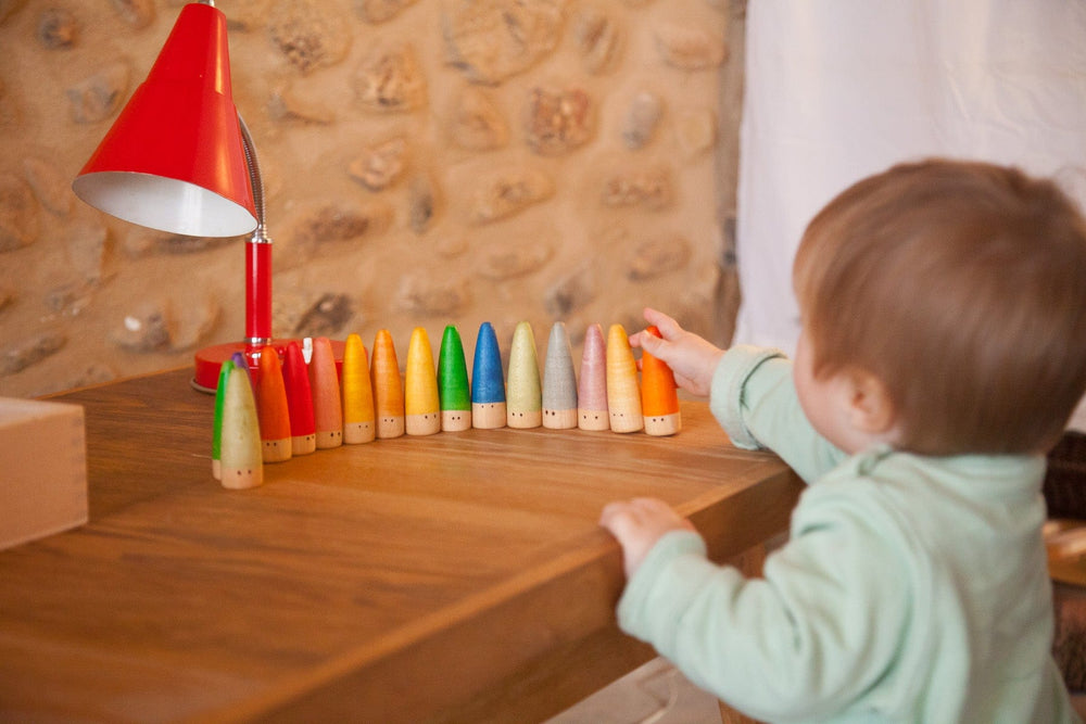 child playing with painted rainbow wooden palos