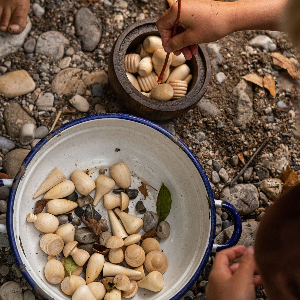 Child outdoors playing with Grapat Mandala Madera Natural loose parts play set in an enamel bowl