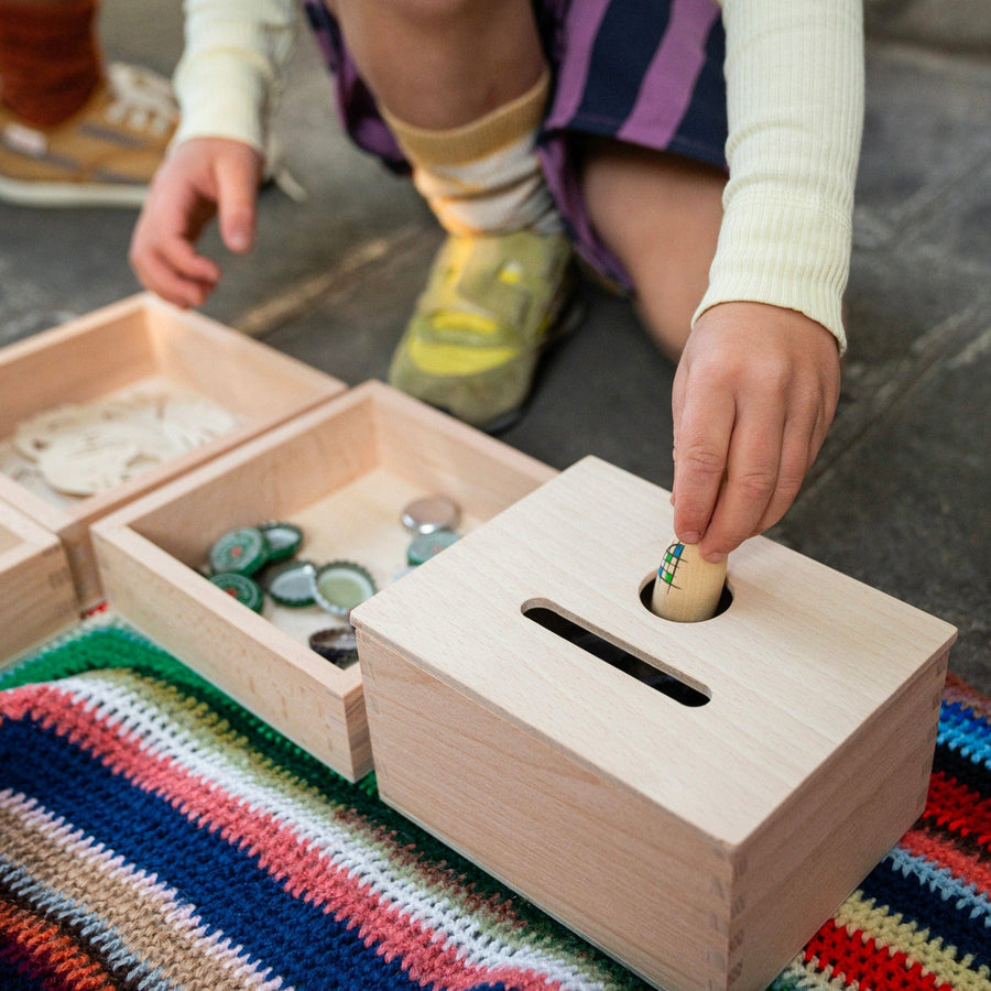 childs hands posting wooden peg dolls in a Montessori inspired object permanence box