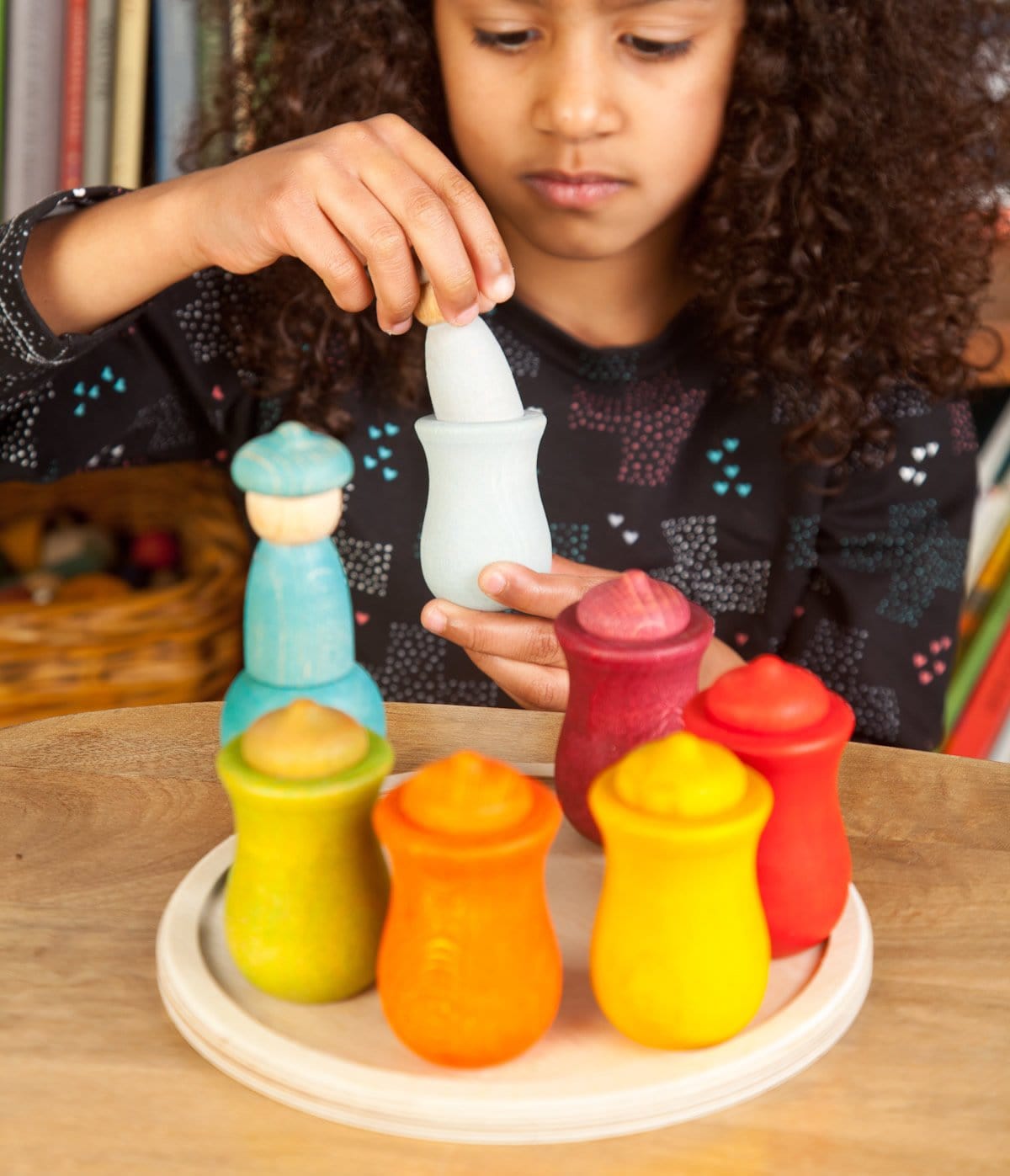 girl playing with Grapat 7 Moons Weekly Calendar  including various colored acorn-shaped figures and cups, displayed on a wooden disk.