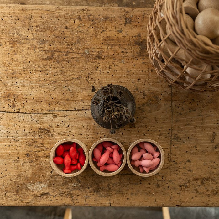 Three small wooden bowls with red and pink contents on a rustic wooden surface.