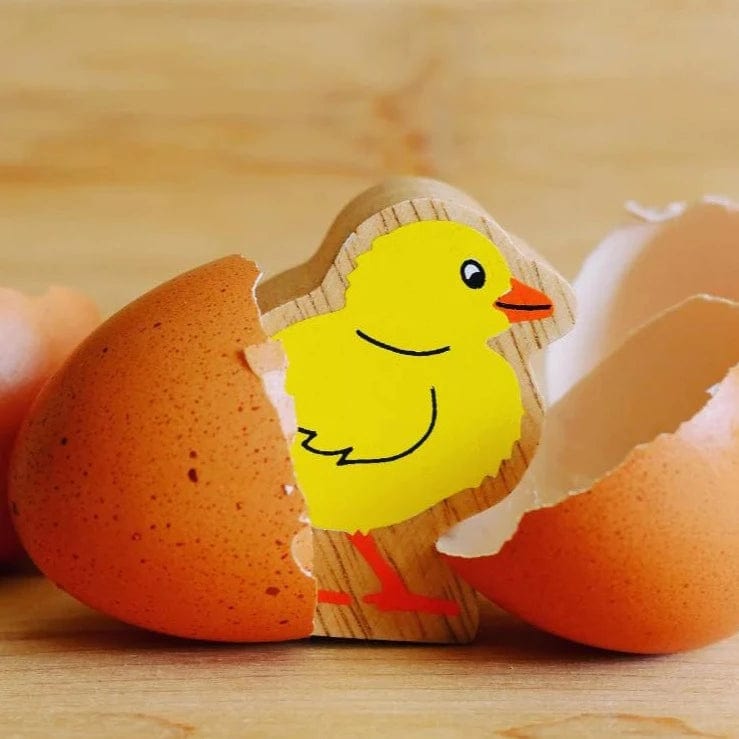 A wooden play figure of a yellow chick with a natural wood grain edge. The play figure is next to an egg shell. 