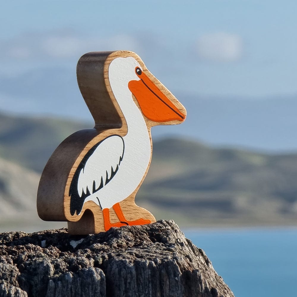 Lanka Kade wooden pelican play figure perched on a rock with a coastal view in the background