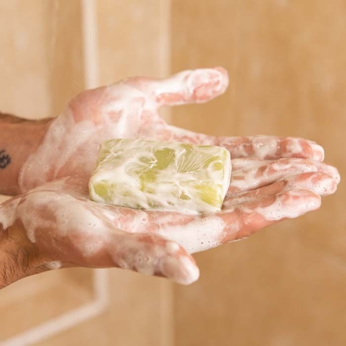 hands holding a bar of solid shower gel in the shower 